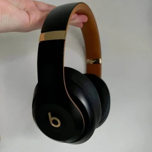 Svarta hörlurar från Beats - Snygga och stilrena svarta hörlurar från Beats med guldiga detaljer. Perfekta för musikälskare som vill ha både bra ljud och en cool look. De är bekväma att bära och har en justerbar bygel för bästa passform.
