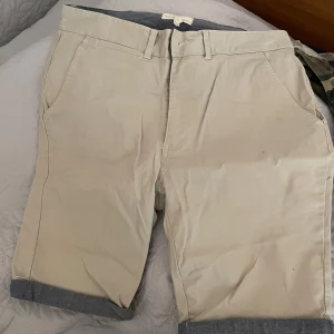 Beige shorts från S.C.W. - Snygga beige shorts från S.C.W. med klassisk design. De har fickor fram och bak med knappar, samt bälteshällor. Perfekta för en avslappnad stil.