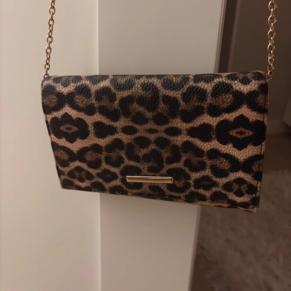 Snygg leopardmönstrad kuvertväska med en elegant guldkedja. Perfekt för att ge din outfit en djärv touch. Väskan har en stilren design och är lätt att bära med sig.. Laukut & Käsilaukut.