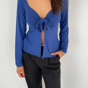 Blå knytblus från design by si - Snygg blå långärmad blus med knytning framtill från design by si. Perfekt för en stilren look med djup v-ringning. Knappt använd och därför i nyskick. Modell Maddy Blouse.