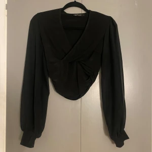 Svart omlottopp från NLY One - Snygg svart omlottopp från NLY One med långa ärmar och en elegant drapering framtill. Perfekt för en stilren look.