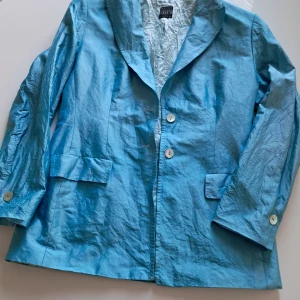 Blå silkesjacka från Ril's - Säljer en elegant blå kavaj från Ril's i 100% silke. Jackan har en klassisk design med knappar framtill och långa ärmar. Perfekt för en stilren look.
