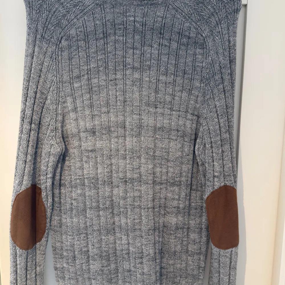 Säljer en stilren grå ribbad kofta från Pier One med knappar framtill och praktiska fickor. Koftan har långa ärmar och bruna armbågslappar som ger en snygg kontrast. . Neuletakit & Villapaidat.