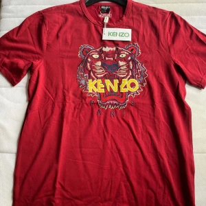 Röd t-shirt med tigerbroderi från Kenzo - Säljer en röd t-shirt från Kenzo med ett stort, färgglatt tigerbroderi på framsidan. T-shirten har korta ärmar och är tillverkad i bomull. Perfekt för dig som vill sticka ut med en djärv design!