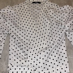 Vitt blus  - Jättefin Vitt blus med svart prickar, den har en kedja. Den är i storlek S ifrån bik bok. Skriv t mig om ni vill ha en bild på hur det ser ut när man har den på🥰