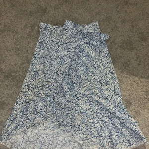 Blommig kjol från Shein - Säljer en söt blommig kjol från Shein i blått och vitt. Kjolen har en volangdetalj och är perfekt för sommarens varma dagar. Den är gjord i ett lätt och luftigt material som ger en skön känsla.