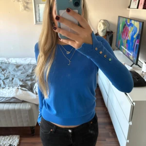 Blå tröja med knappar - Snygg blå tröja från Zara med långa ärmar och dekorativa knappar vid ärmsluten. Perfekt för en stilren look.