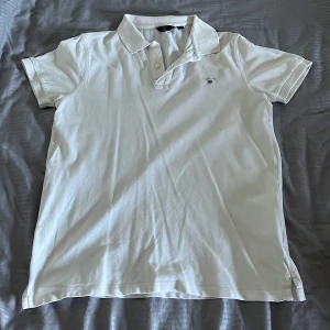 Vit kortärmad pikétröja från GANT - Säljer en klassisk vit pikétröja från GANT med korta ärmar och knappar vid kragen. Perfekt för en stilren och avslappnad look. Tröjan har en liten broderad logga på bröstet.