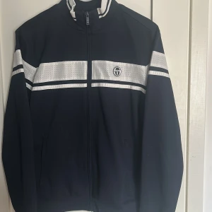 Zip från Sergio Tacchini - Snygg hel-zip från Sergio Tacchini. Mörk blå med vita detaljer. Använd en gång, inget slitage. Storlek L men passformen är mer M/L.