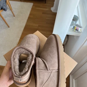 Bruna boots från UGG - Säljer ett par mysiga bruna boots från UGG. De är tillverkade i mocka och har en mjuk pälsfodring för extra komfort. Perfekta för kyliga dagar.