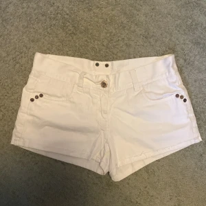 Vita shorts mini shorts low waist - Snygga vita shorts med dekorativa nitar på fickorna. De har en knappstängning fram och är perfekta för sommardagar. Passar bra till en avslappnad stil. <— skrivet av Plick ai 😀, de är storlek xs märke East west