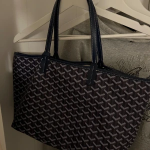 Mönstrad axelväska i blått och vitt - Snygg axelväska med ett klassiskt mönster i blått och vitt. Väskan har två långa handtag och är perfekt för att bära med sig allt man behöver. Den har en stilren design som passar till många olika outfits.