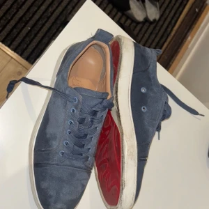 Blå sneakers med röd sula - Snygga blå sneakers i mocka med en iögonfallande röd sula. Skorna har snörning och en klassisk design som passar perfekt för en stilren look. Äkta loubitins som är köpt för två år sedan i frankrike. Säljs för att jag inte använder dessa mer, använt under bröllop och större fester bara. 