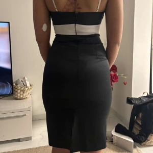 Svart och vit klänning - Elegant svart och vit klänning med axelbandslös design. Klänningen har en tight passform. Perfekt för en stilren look.