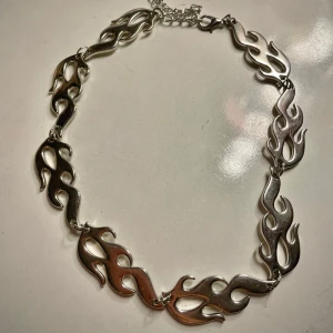 Silverfärgat halsband med flammönster - Unikt silverfärgat halsband med ett coolt flammönster. Halsbandet har justerbar kedja och karbinhake för enkel användning. Perfekt för att ge din outfit en edgy touch.