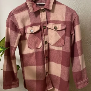 Rutig overshirt från H&M - Säljer en snygg rutig overshirt från H&M i rosa och beige. Skjortan har långa ärmar och knappar framtill samt två bröstfickor med knappstängning. Perfekt för lager-på-lager-stil. Hade på mig den bara 4 gånger!🎀🩷