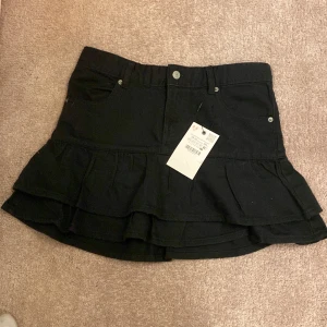 Svart kortkjol med volang - Intressekoll på en Snygg svart jeans kortkjol med volangdetaljer. Kjolen har en klassisk design med fickor och bälteshällor, perfekt för en trendig look. Från Zara stl 164 (13-14) men jag skulle säga att den passar typ xs - s. Använd 1 gång!!❣️❣️(prislappen är INTE kvar ⚠️⚠️)