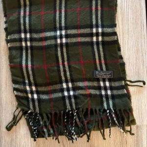 Grön burberry scarf -  Snygg grön rutig halsduk från Burberry med klassiskt mönster i rött, svart och vitt. Tillverkad i mjukt material med fransar i ändarna.  Använd 2 gånger 8/10 i skick