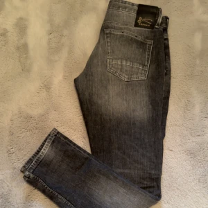 Grå jeans från Denham - Snygga grå jeans från Denham med en lätt slitning för en cool look. De har en klassisk femficksdesign och knappgylf. Perfekta för en avslappnad stil.