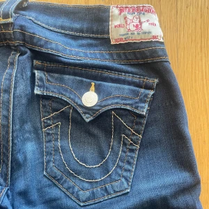 Mörkblå jeans från True Religion - Äkta jeans från True Religion med snygga bakfickor och kontrastsömmar. Jeansen är omsydda till bootcut. De är i bra skick men finns små märken vid insidan högst upp, (se bild). Skriv privat för fler bilder och frågor❤️