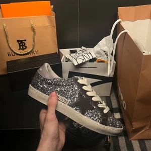 Golden Goose Superstars - Unika och stiliga Golden Goose Superstars i en fantastisk kombination av glitter och brunt! Dessa skor i storlek 38 är perfekta för både vardag, fest och för dig som vill ha något extra. Med sin trendiga design ger de ett lyft till varje outfit och passar både till avslappnade och mer festliga tillfällen. Tveka inte att höra av dig om du har några frågor eller funderingar – vi ser fram emot att höra från dig! OBS box och kvitto ingår ej 