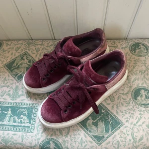 Vinröda sneakers från Alexander McQueen - Snygga vinröda sneakers från Alexander McQueen i mocka. Dessa är så otroligt coola och så snygga nu till våren. Mönstret där bak ska vara ”fläckigt” så det är inte smutsigt! Nypris ligger runt 6000kr❤️Hör av dig vid intresse