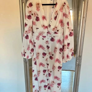 Vit blommig klänning  - Säljer en vacker vit klänning blommor. Klänningen har långa ärmar och en djup v-ringning. Perfekt för till midsommar! Slutsåld på hemsida och i butik 