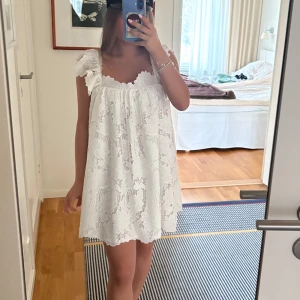 Vit spetsklänning med volangärmar - Supersöt vit kortklänning i spets med volangdetaljer på axlarna. Klänningen har en lös passform och är ärmlös med romantiska volanger. Perfekt för sommarens alla tillfällen men främst studenten🫶🏻🐬🫧🌸🎀Prislappen sitter kvar och är helt slutsåld💞😛💖🌞