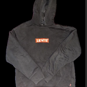 Svart hoodie från Levi's med logga - Säljer en svart hoodie från Levi's i storlek S med klassisk röd och vit logga på bröstet. Tröjan har huva med dragsko och en stor magficka. Perfekt för en avslappnad och cool stil. Priset kan diskuteras  