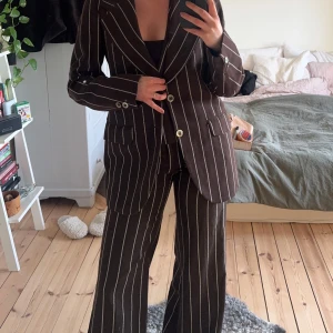 3 set kostym - Brun kostym med vita ränder , väst, byxor och kavaj. figursydd modell med vida axlar i kavajen. Västen är också figursydd samt byxorna har utsvängda ben. Snygga att använda var för sig, eller alla tillsammans. Har tyvärr växt ur denna snygga kostym.  Säljs alla delar endast ihop