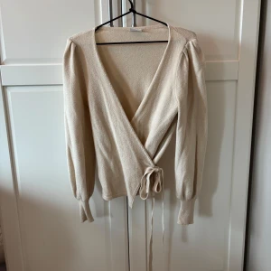 Beige omlottkofta från VILA - Säljer en beige omlottkofta från VILA i storlek XS. Koftan har långa ärmar, knytband i midjan och är stickad i ett mjukt material. Perfekt för lager-på-lager och enkel att styla till olika outfits. Passar jätte bra med ett par jeans. 