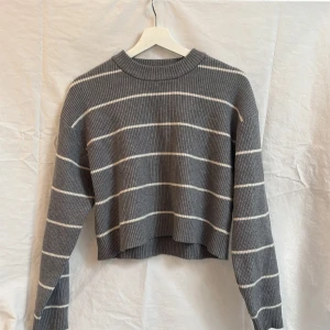 Grå randig croppad stickad tröja från Zara - Grå stickad tröja med vita horisontella ränder. Modellen är croppad med lång ärm och rund halsringning. Storlek 164