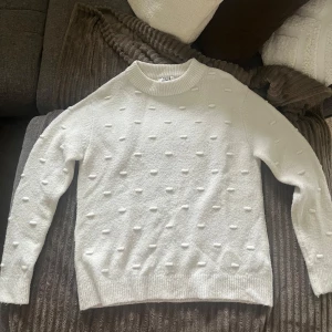 Vit stickad tröja från NAKD - Säljer en vit stickad tröja från Nakd med upphöjt prickigt strukturmönster. Tröjan har rund halsringning och långa ärmar. Perfekt för lager-på-lager. Säljer för 100kr🫶🏼