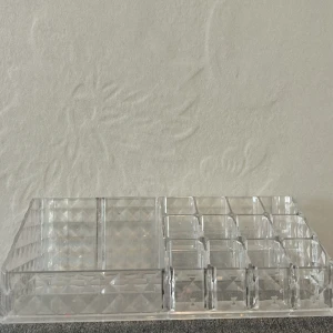 sminkorganiserare - Praktisk sminkorganiserare i transparent akryl med flera fack i olika storlekar. Perfekt för att förvara läppstift, borstar, pennor och andra sminkprodukter. Stilren design med rutmönster på sidorna.
