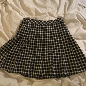 Svartvit rutig kjol från H&M - Säljer en svartvit rutig kjol från H&M. Kjolen har klassiskt rutigt mönster, är kort och har en lätt utställd passform. Perfekt för dig som gillar en preppy stil. Stängs med dragkedja i sidan.
