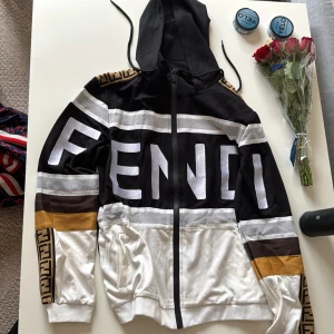 Fendi byxor med logoband - Snygga Fendi byxor i svart, vitt och gult med breda logoband längs sidorna. Byxorna har resår i midjan och mudd vid benslut. Perfekta för en trendig och sportig look.