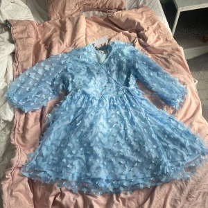 Ljusblå klänning med fjärilar  - Superfin ljusblå klänning från Noella med 3D-fjärilar som fladdrar lite när man rör på sig, kjol i tyll. Aldrig använd och har slutat säljas, så exklusiv! Originalpris 1200kr. Klänningen har omlottmodell, knyt i midjan och trekvartsärmar. Storlek XXL med kan bli nån storlek mindre eller större pga omlottfunktionen. Perfekt för sommarens tillfällen när du vill sticka ut lite extra.
