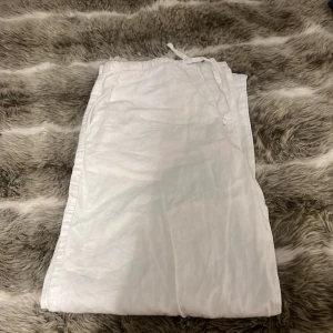 Vita linnebyxor med dragsko från Gina Tricot - Säljer ett par vita linnebyxor från Gina Tricot med elastisk midja och dragsko. Byxorna har en avslappnad passform och är perfekta för varma dagar. Luftigt material som känns svalt mot huden.