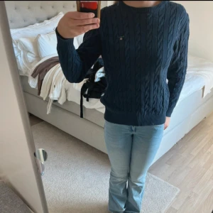 Mörkblå grov- kabelstickad tröja från GANT - Säljer en grovstickad mörkblå kabelstickad tröja från GANT med rund halsringning och diskret broderad logga på bröstet. Tröjan har långa ärmar och ribbade muddar vid ärmslut och nederkant. 