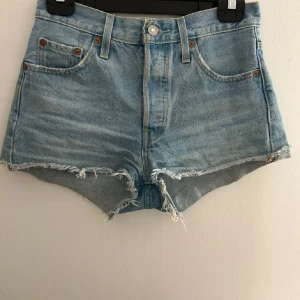 Ljusblå jeansshorts från Levi's 501 - Ljusblå jeansshorts från Levi's 501 med råa, fransiga kanter och klassisk femficksdesign. Hög midja och knappgylf. Perfekta för sommaren och har en avslappnad, vintagekänsla. Köpts för 1000kr och säljer för de är för små för mig och för att jag ska kunna köpa min balklänning. Pris kan diskuteras vid snabbt köp 