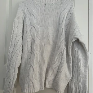 Vit stickad tröja med flätmönster från 157 - Säljer en vit stickad tröja från 157 med snyggt flätmönster längs ärmar och fram. Tröjan har rund halsringning och långa ärmar. Perfekt för kyliga dagar och enkel att matcha med jeans eller kjol.