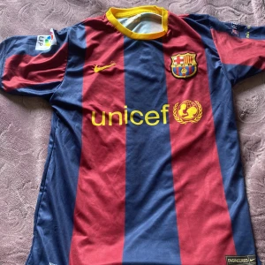 FC Barcelona fotbollströja Nike - Säljer en klassisk FC Barcelona fotbollströja från Nike med breda blå och röda ränder, gul krage och Unicef-tryck på bröstet. Broderad klubbmärke på vänster bröst. Dri-FIT-material för bra andningsförmåga.