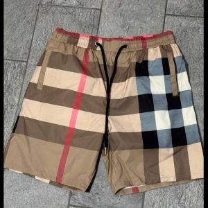 Burberry shorts - Snygga shorts i klassiskt beige, svart och rött rutmönster från Burberry. De har elastisk midja med svart snörning och sidofickor samt en bakficka. Perfekta för sommaren med sin lätta och bekväma känsla.  L MEN PASSAR MER M ÄN L