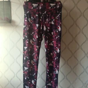 Mönstrade träningstights  - Säljer ett par snygga träningstights med blommigt mönster i lila, vinrött, svart och vitt. Tightsen har hög midja och är i stretchigt syntetmaterial som passar perfekt till gymmet eller löprundan. Väldigt bekväma men tyvärr försmå för mig!! 60kr 