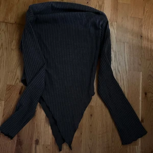 Grå ribbad långärmad topp - Säljer en grå ribbad långärmad topp med asymmetrisk nederkant. Tröjan har en tight passform och är perfekt för att skapa en snygg och trendig look. Passar till både jeans och kjol.
