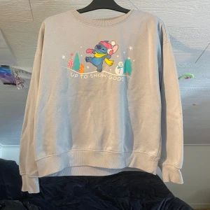 Ljusblå sweatshirt med Stitch från Disney - Säljer en ljusgblå sweatshirt från Disney med ett tryck av Stitch som åker skridskor och texten 'Up to snow good'. Tröjan har rund hals och långa ärmar. Perfekt för dig som älskar Disney och vill ha en mysig tröja med vintertema.