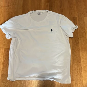 Vit t-shirt från Polo Ralph Lauren - Klassisk vit t-shirt från Polo Ralph Lauren med rund halsringning och broderad marinblå logga på bröstet. Tillverkad i mjuk bomull och har en normal passform. Perfekt basplagg för garderoben.