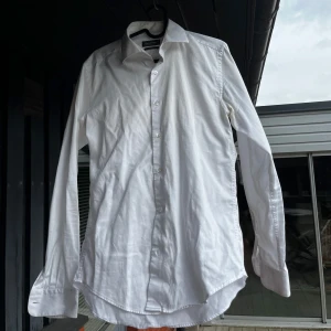 Vit skjorta med lång ärm - Klassisk vit skjorta med lång ärm och knappar framtill. Skjortan har en tidlös design och passar perfekt till många olika tillfällen. Slim fit från dressman, använd ca 3 gånger