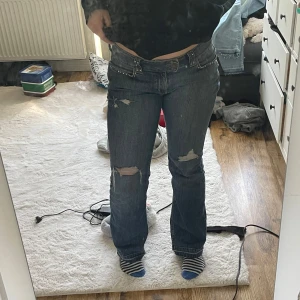 lågmidjade bootcut jeans med slitningar - Säljer ett par blå bootcut jeans med slitningar och fina detaljer. Jeansen har låg midja.  Dom har gått sönder lite längst ner för att jag har gått på dom och det saknas även lite stenar. Storleken i jeansen är 40 men skulle säga att dom är lite mindre. Pris kan diskuteras!!!