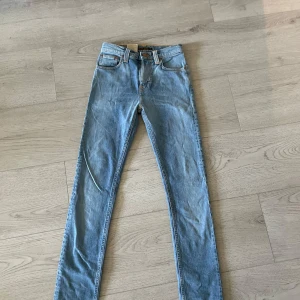 Nudie Jeans High Kai ljusblå jeans - Säljer ett helt nytt par Nudie Jeans High Kai i ljusblå tvätt, modell 'Used Light Indigo'. Klassisk femficksdesign, orange sömmar och smal passform. Perfekta för dig som gillar stilrena och tidlösa jeans med snygga detaljer.